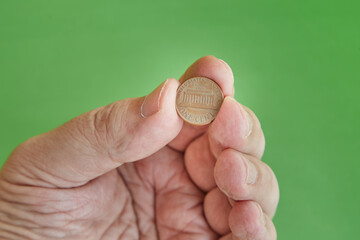 One cent coin in hand on a green background close-up, one cent in hand, minimum bet, minimum payment