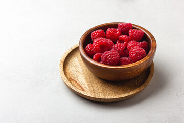 Fresh raspberries in a wooden bowl on a light grey background