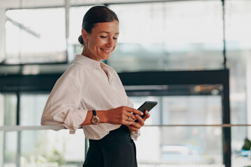 A Smiling Businesswoman is Engaged with her Smartphone while in a Modern Work Environment