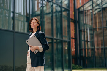 A confident businesswoman is working on a laptop outside a contemporary office building