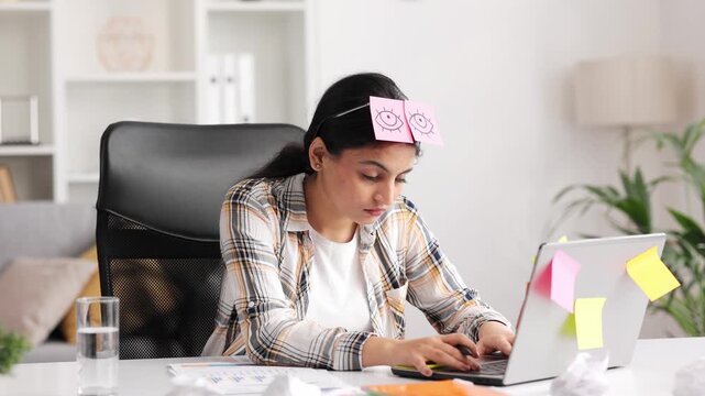 Tired young Indian girl falls asleep at workplace from overwork. A female student sleeps with stickers on her eyes while studying.