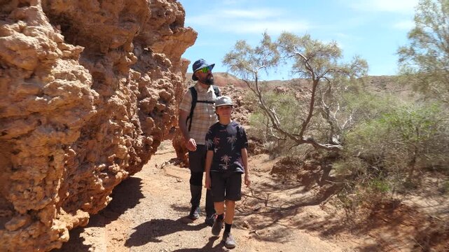 Father and son traveling in a wild, arid area among unusual rocks. Desert area with yellow sandstone cliffs. Family trip. Boguty mountains. Kazakhstan. 2x slow motion