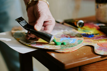 Closeup of hand of unrecognizable artist squeezing green oil paint from tube onto palette