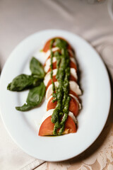 delicious dish of fresh tomatoes and tasty mozzarella with aromatic herbs under a creamy spinach sauce in a beautiful white plate on a wooden table in a cozy and nice restaurant