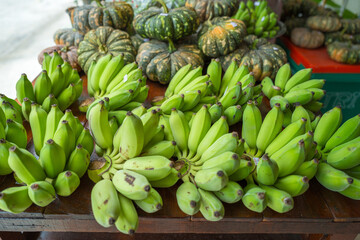Raw bananas in green color and pumpkins put on merchandise shelf for selling.