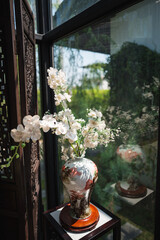 The ancient chinese style vase with artificial white flowers in the glass corner.
