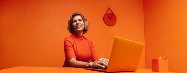 Mature woman providing customer support in vibrant monochrome orange office setting with copy space
