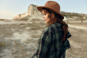 Woman in plaid shirt and hat gazes into distance in desert landscape with a sense of contemplation