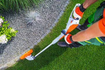 Person Trimming Grass Edges With String Trimmer in a Garden on a Sunny Day