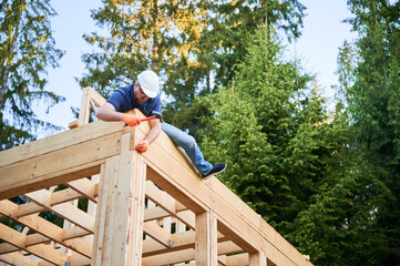 Woodworker constructing wooden, two-story frame-built house near the woods. Bearded, spectacled man...