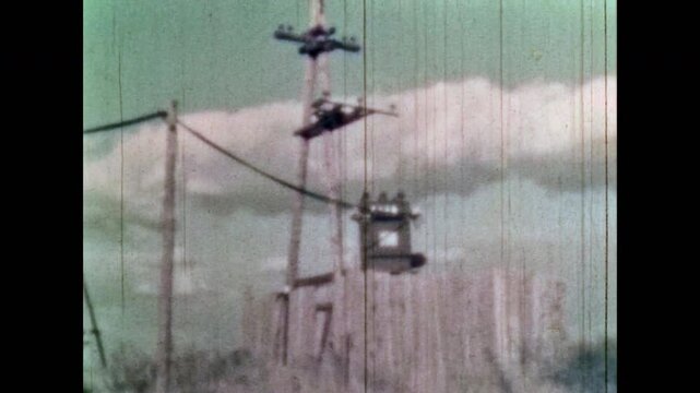 Archive film, Utility workers maintain high voltage power lines on electric poles on sky backdrop. Old electric technology in nature. Electricity infrastructure. Retro 1960s. Obsolete equipment