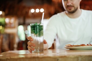 With mojito. Man is sitting in the restaurant and eating a pizza