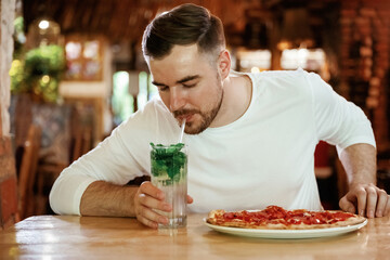 With mojito. Man is sitting in the restaurant and eating a pizza