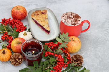 Autumn still life with a cup of hot coffee, blueberry pie, candle, pumpkins and rowan berries. Sweet homemade seasonal pie on a table. 