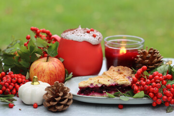 Autumn still life with a cup of hot coffee, blueberry pie, candle, pumpkins and rowan berries. Sweet homemade seasonal pie on a table. 