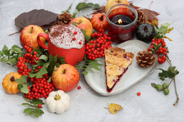 Autumn still life with a cup of hot coffee, blueberry pie, candle, pumpkins and rowan berries. Sweet homemade seasonal pie on a table. 