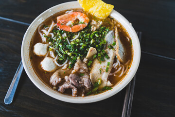 Tom Yum soup - Thai soup with prawns and rice noodles on wooden table in Vietnam