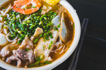 Tom Yum soup - Thai soup with prawns and rice noodles on wooden table in Vietnam