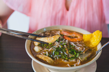 Tom Yum soup - Thai soup with prawns and rice noodles on wooden table in Vietnam