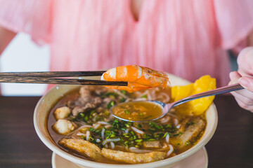 Tom Yum soup - Thai soup with prawns and rice noodles on wooden table in Vietnam