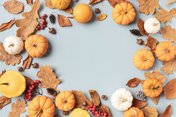 Autumn frame from fall leaves, pumpkins and seasonal decorations on turquoise background top view.