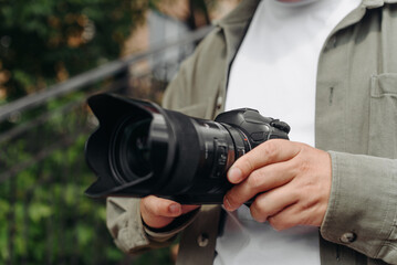 dslr camera in hands, young adult caucasian photographer in white t-shirt at work outdoors in sunny summer day