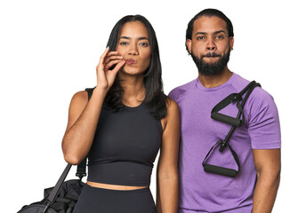 Young Latino couple ready for gym training with fingers on lips keeping a secret.
