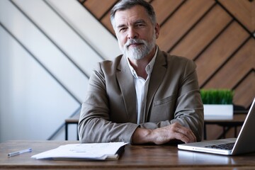Naklejka premium Smiling mature business man executive wearing shirt sitting at desk using laptop. Happy busy professional middle aged manager investor working on computer in office