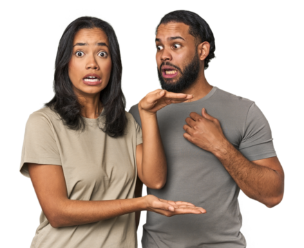 Young Latino couple in studio shocked and amazed holding a copy space between hands. - Powered by Adobe