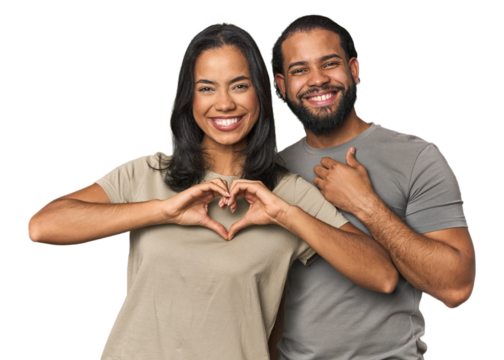 Young Latino couple in studio smiling and showing a heart shape with hands.