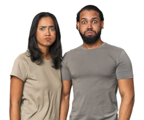 Young Latino couple in studio blows cheeks, has tired expression. Facial expression concept.