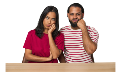 Seated young Latino couple at table who feels sad and pensive, looking at copy space.