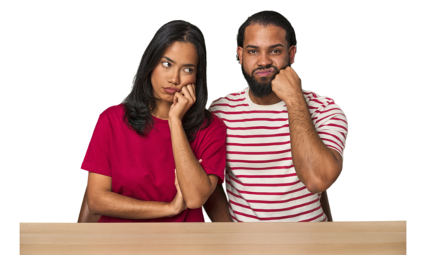 Seated young Latino couple at table who feels sad and pensive, looking at copy space.