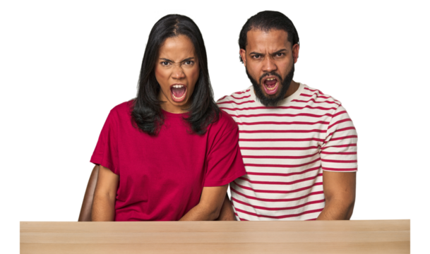 Seated young Latino couple at table shouting very angry, rage concept, frustrated.
