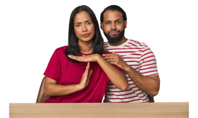 Seated young Latino couple at table showing a timeout gesture.