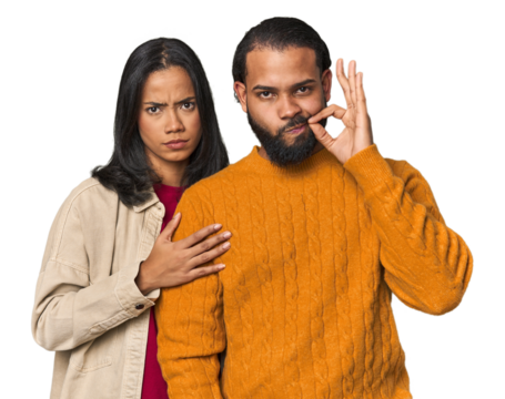 Young Latino couple in studio with fingers on lips keeping a secret.