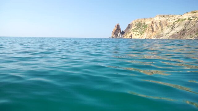 Sea water surface. Camera flies over the calm azure sea with volcanic rocky shores on background. Nobody. Holiday recreation concept. Abstract nautical summer ocean nature. Slow motion. Close up