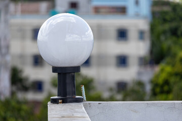White round glass lamp on a black steel pole on white wall in house rooftop, blur background.