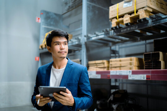 A man in a blue suit holding a tablet in front of a warehouse. He is looking at the tablet and he is focused on the content displayed