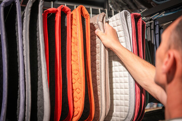 Selecting Colorful Horse Saddle Pads in a Tack Shop During Daylight