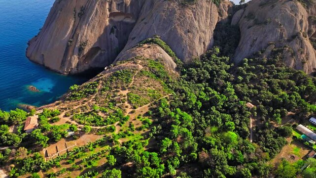 Aerial view of a Botanical garden with Snug Cove framed by rugged cliffs in Parc du Mugel. View from above of swimming off a pebble beach with turquoise clear water in France.