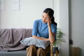 Fototapeta premium Young Woman Sitting on Sofa Looking Thoughtful and Pensive in a Modern Living Room