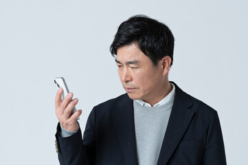 スマートフォンを見てネガティブな表情をする50代男性