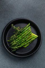 Asparagus with thyme in a black plate on a dark background