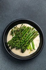 Asparagus with creamy sauce in a black bowl on a dark background