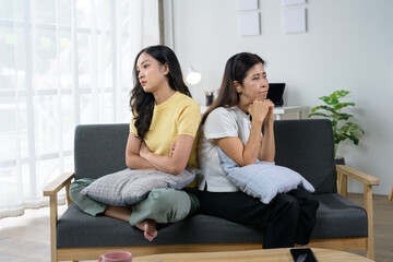 Mother and Daughter Sitting on Sofa in Living Room, Facing Away from Each Other, Looking Upset and Thoughtful