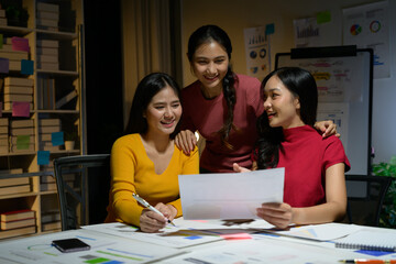 Three Young Women Collaborating on a Project in a Modern Office Setting with Charts and Graphs