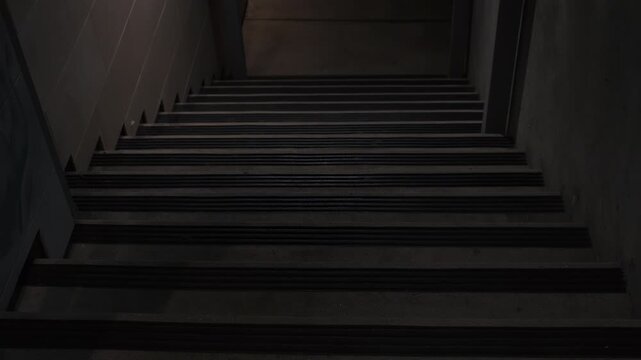 Tilt shot of dimly lit stairs going down to metal grate. Staircase leading down to metal grate door, the light is faint and dim.