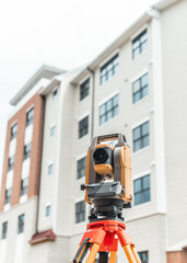 land surveying total station instrument on a tripod with a building in the background