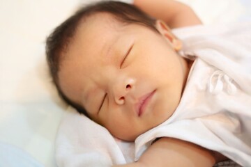 A newborn baby is sleeping on a white mattress.